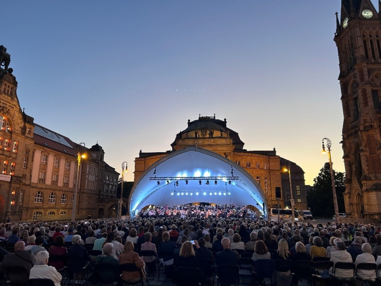 An open-air stage on Theatre Square with hundreds of guests in the evening.