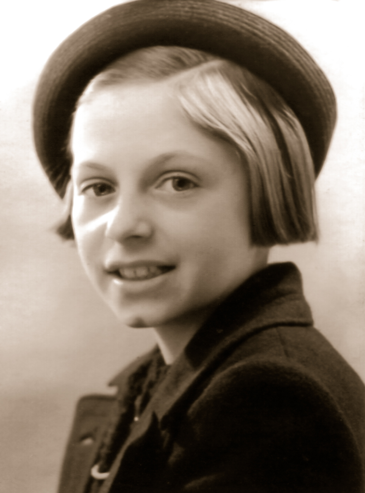 Das Foto zeigt ein elfjähriges Mädchen. Sie hat halblange blonde Haare und trägt eine Jacke mit Kragen sowie einen schräg auf dem Kopf sitzenden dunken Hut.